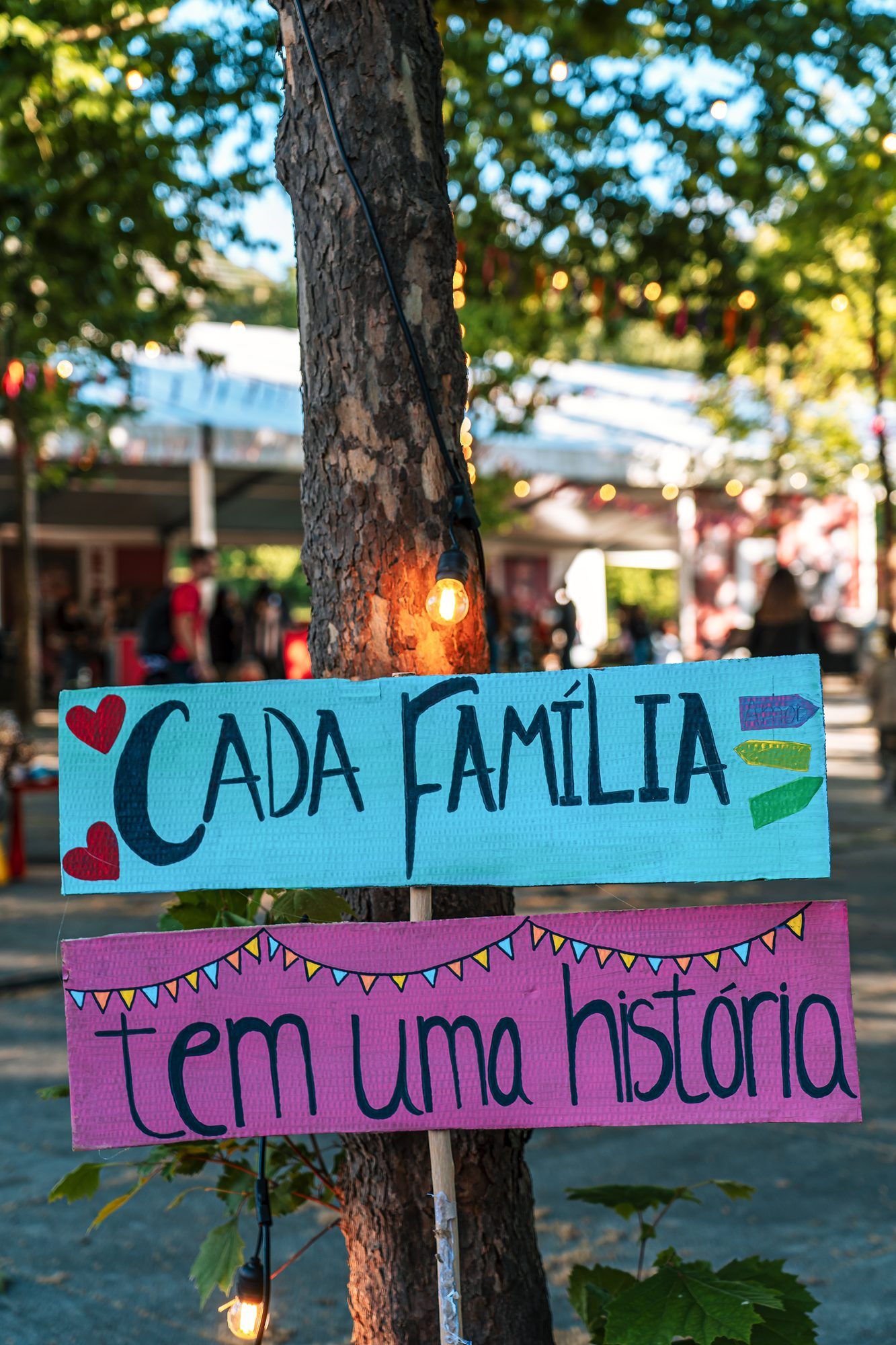 Placas pintadas à mão numa árvore com a frase «Cada família tem uma história»